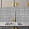 A kitchen countertop with a white sink and light gray subway tiles and wooden cabinet hardware.