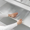 A hand is applying self-adhesive aluminum foil wall decals to a white cabinet surface.