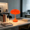 Una lámpara de escritorio esférica naranja con un tallo delgado sobre una superficie de escritorio blanca.
