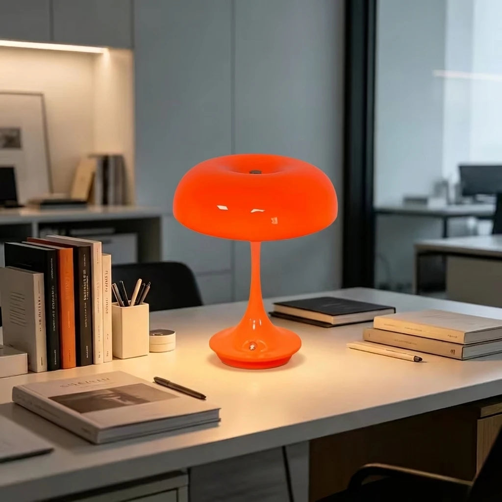 Una lámpara de escritorio esférica naranja con un tallo delgado sobre una superficie de escritorio blanca.