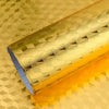 A roll of self-adhesive aluminum foil wall decals with a textured, gold finish lying on a reflective surface.