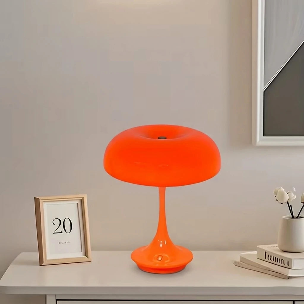 Una lámpara de escritorio naranja y brillante con base cónica sobre una mesa blanca contra una pared gris claro.