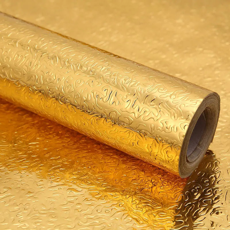 Roll of self-adhesive aluminum foil wall decals lying on a reflective gold surface.