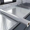 Roll of silver self-adhesive aluminum foil wall decals placed on a kitchen countertop next to a stainless steel sink.