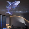 Proyector LED multicolor que muestra la silueta de una ballena azul brillante contra un cielo estrellado en el techo.