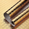 Roll of gold patterned self-adhesive aluminum foil wall decals lying on a textured surface.