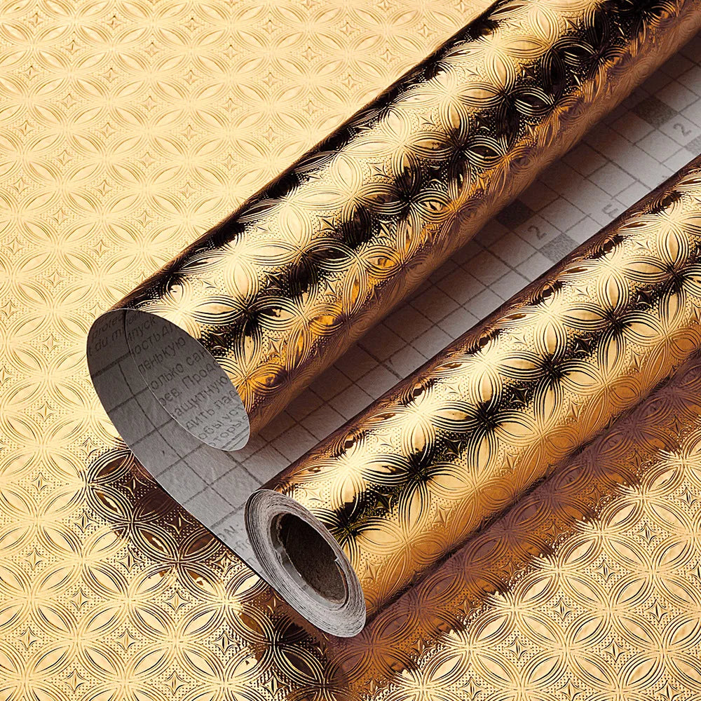 Roll of gold patterned self-adhesive aluminum foil wall decals lying on a textured surface.