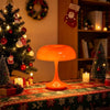 Una lámpara de escritorio naranja con pantalla abombada sobre una mesa festiva navideña.