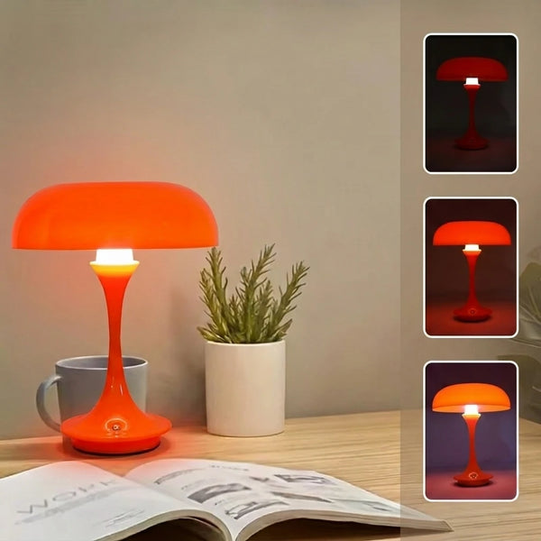 An orange desk lamp with a smooth shade and stem sits on a wooden surface next to an open book.