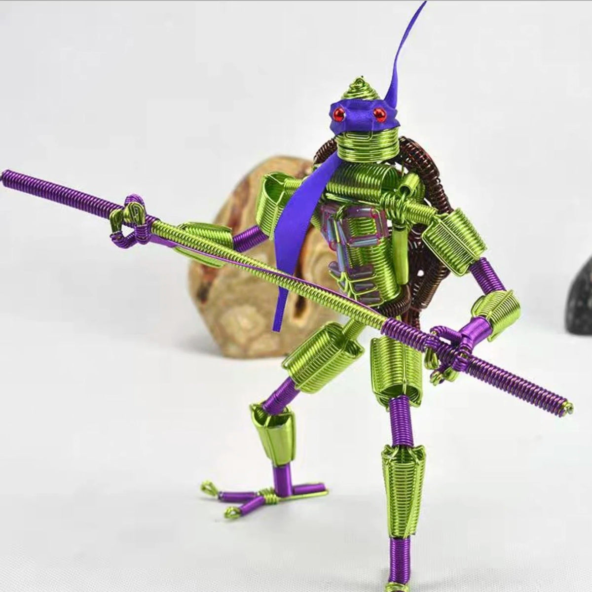 Detaillierte Miniaturfigur eines stilisierten Insekts oder Wesens aus anodisiertem Metall-Kabelwerk in violetten und grünen T