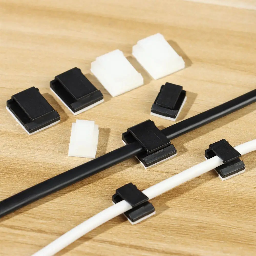 Black self-adhesive cable clips with white foam insulation are shown on a wooden surface.