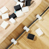 Self-adhesive cable clips in black and white are arranged along a black wire on a wooden surface.