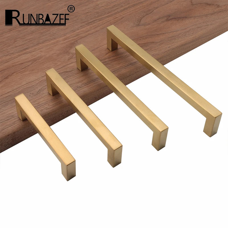 Three modern golden brass cabinet handles displayed on a wooden surface.