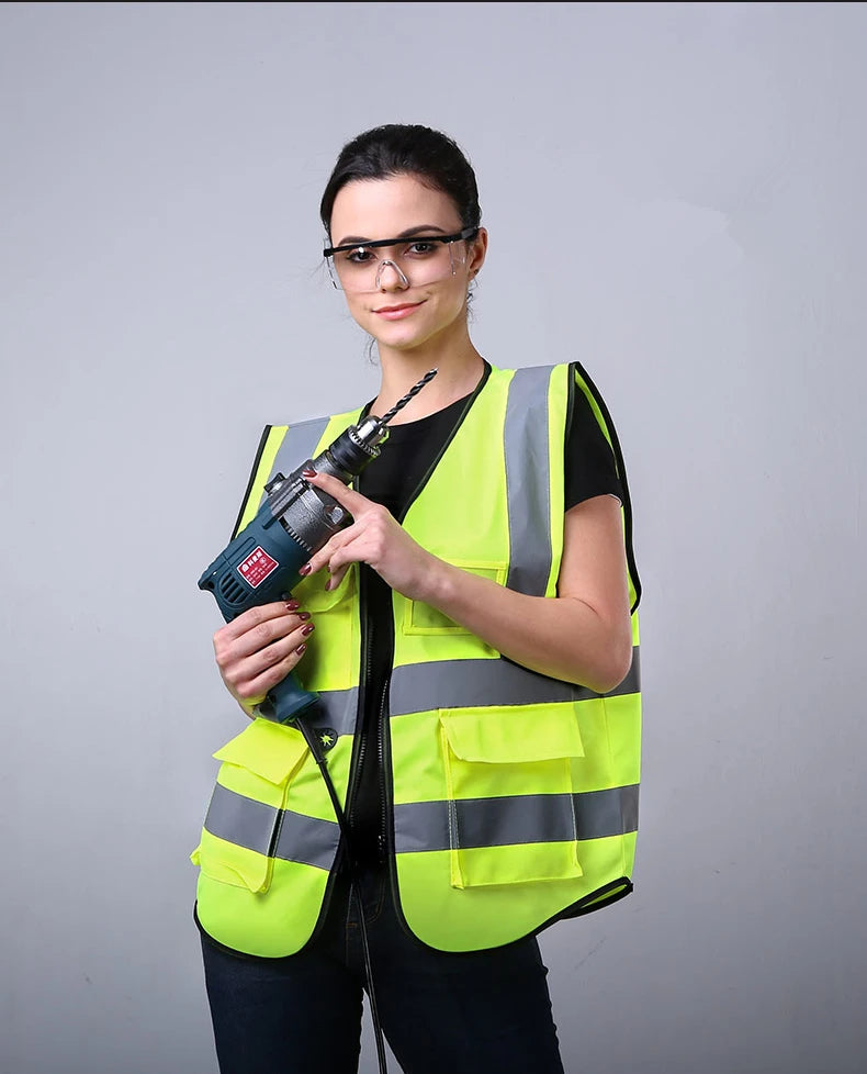 A woman wearing a neon yellow high-visibility safety vest and glasses holds a black tool.