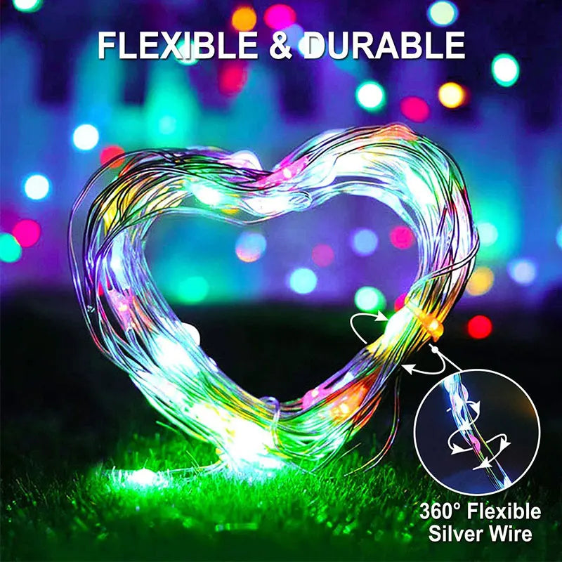 A heart-shaped flexible silver wire light decoration glowing brightly on green grass.