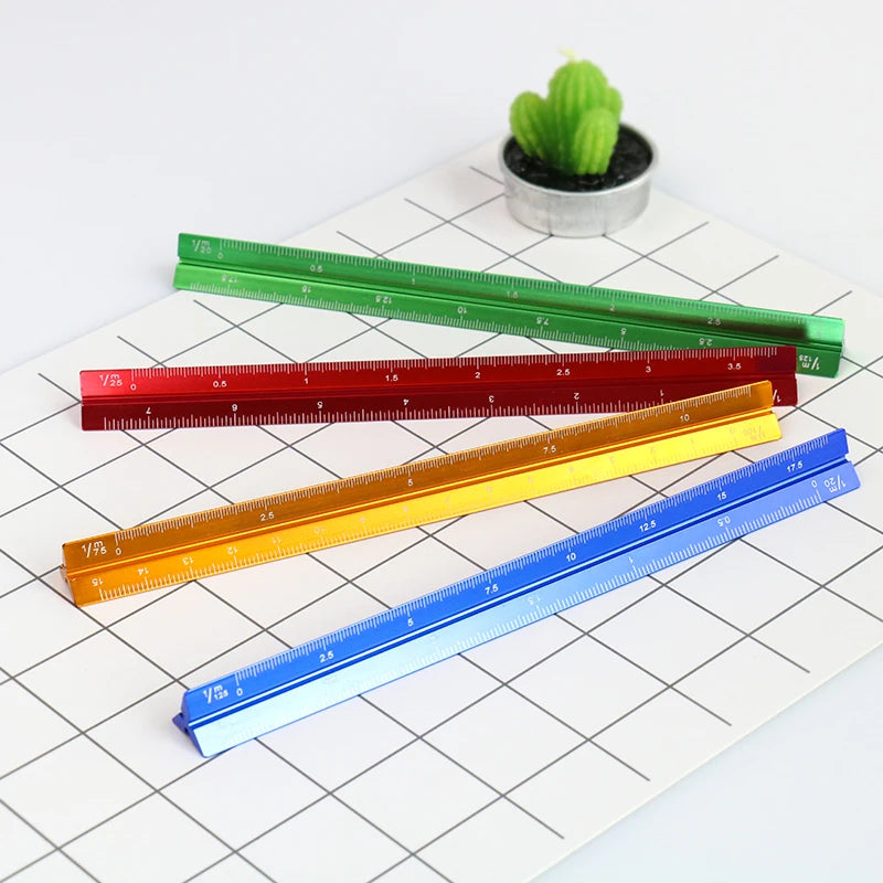 A collection of colorful aluminum triangular rulers laid on a white grid paper next to a small green cactus.