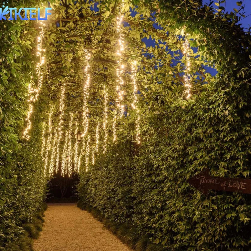 Üppiger grüner Hecke tunnel, beleuchtet von vertikalen Reihen warmer weißer LED-Lichter.