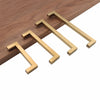Four modern golden brass cabinet handles laid diagonally on a wooden surface.