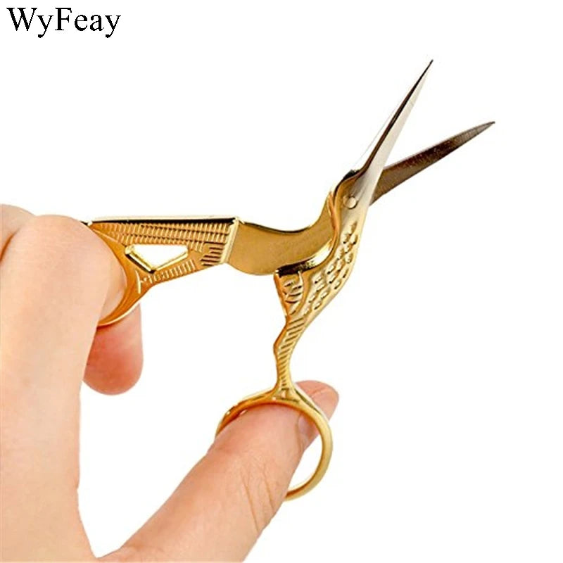A pair of vintage floral embroidery tailor scissors in gold color being held by a hand.