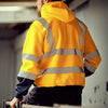 Back view of a man wearing a yellow reflective winter zipper hoodie in a factory or industrial setting.