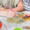 Hands are painting a detailed picture on paper using various tools and paints.