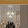 A modern crystal chandelier lamp with three glass globes hangs above a dark table in a well-lit room.