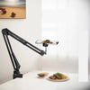 A black professional overhead lighting phone tripod is mounted on a white table, illuminating food.