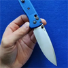 A hand holds a blue lightweight folding pocket knife with a silver blade against a blue background.