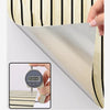 A hand is measuring the thickness of a self-adhesive wood grain wall panel, which features vertical stripes.