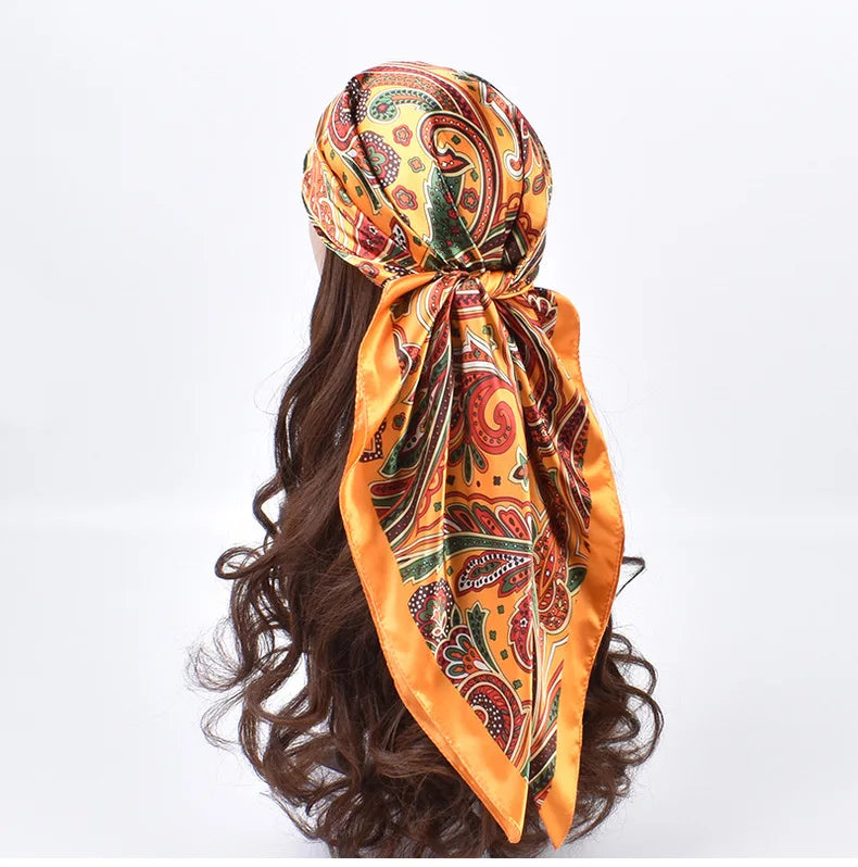 Foulard hijab en satin soie orange vif avec motifs paisley et floraux, noué autour d'une chevelure brun foncé.