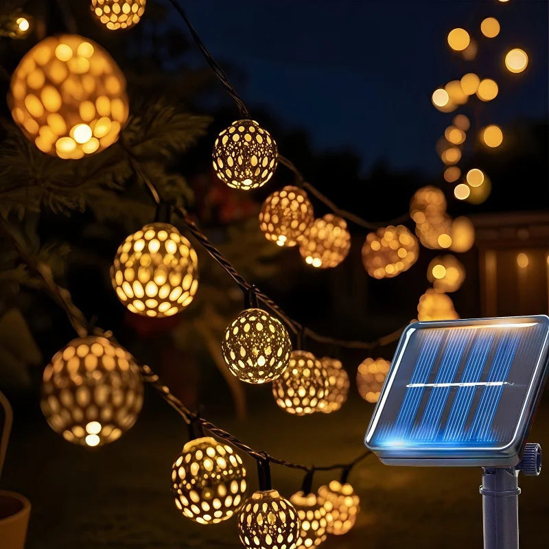 Luces de cuerda marroquíes brillando en una rama oscura de árbol con un panel solar cerca