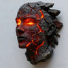 A dark, cracked resin sculpture of a human head glowing with internal orange and red light.