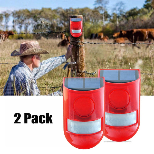 A pair of red solar infrared motion sensor security alarms mounted on wooden posts in a rural field.