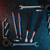 A collection of various metal tools and components including wrenches, drill bits, and magnetic grippers on a dark surface.