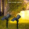 Zwei schwarze Solarlampen beleuchten eine grasbewachsene Fläche neben einem großen Felsen und Laubwerk.