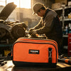 A man working in a workshop is holding an orange tool bag on a wooden surface.