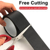 A hand is using scissors to cut a roll of black carbon fiber protection tape for car protection.
