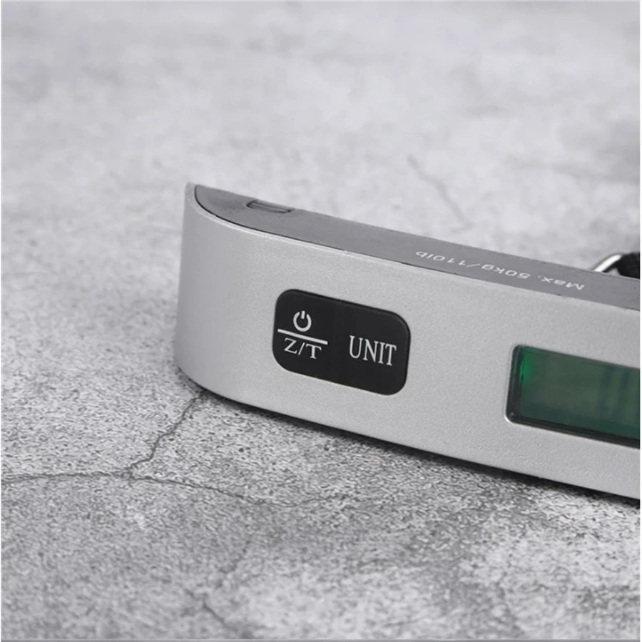 A silver portable digital luggage scale with a display showing Z/T UNIT markings resting on a gray surface.