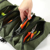 Eine Hand öffnet eine grüne Stofftasche mit verschiedenen kleinen Werkzeugen und Gadgets.