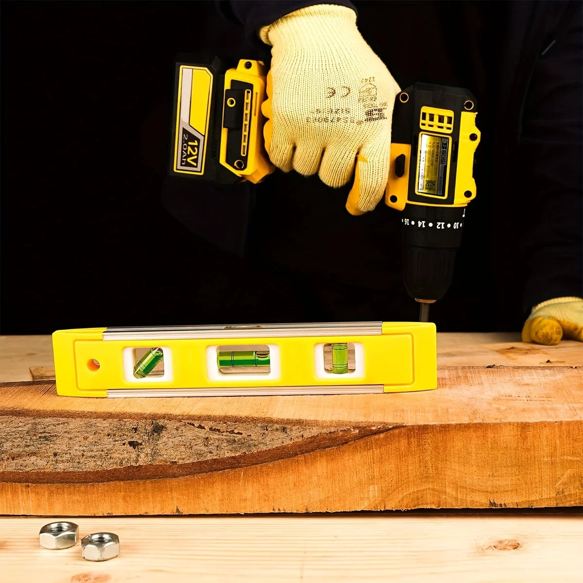 A hand wearing a yellow glove holds a precision magnetic box level next to a wooden surface.