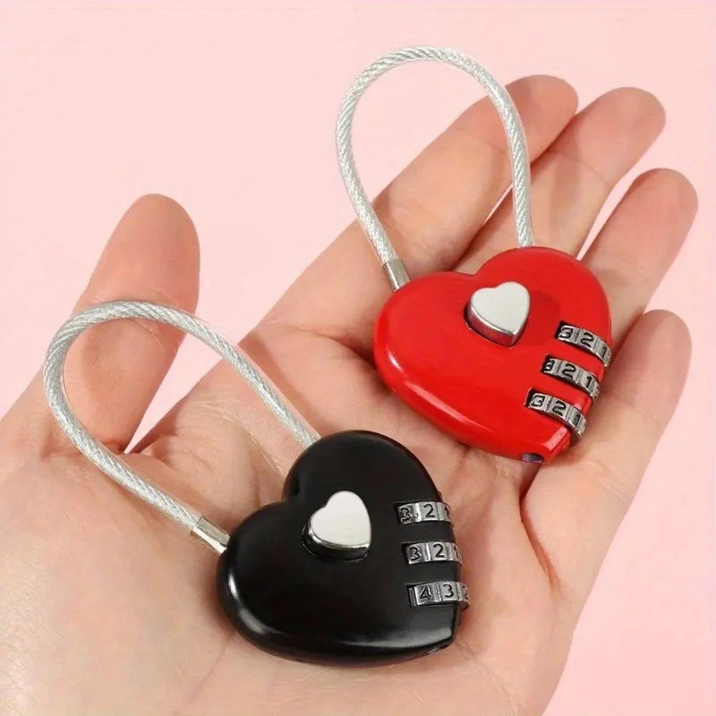 A hand holds a compact heart-shaped combination padlock in red and black with silver wire loops.