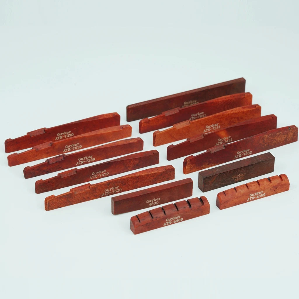 A collection of acoustic guitar bone bridge saddles in various shades of reddish-brown wood.
