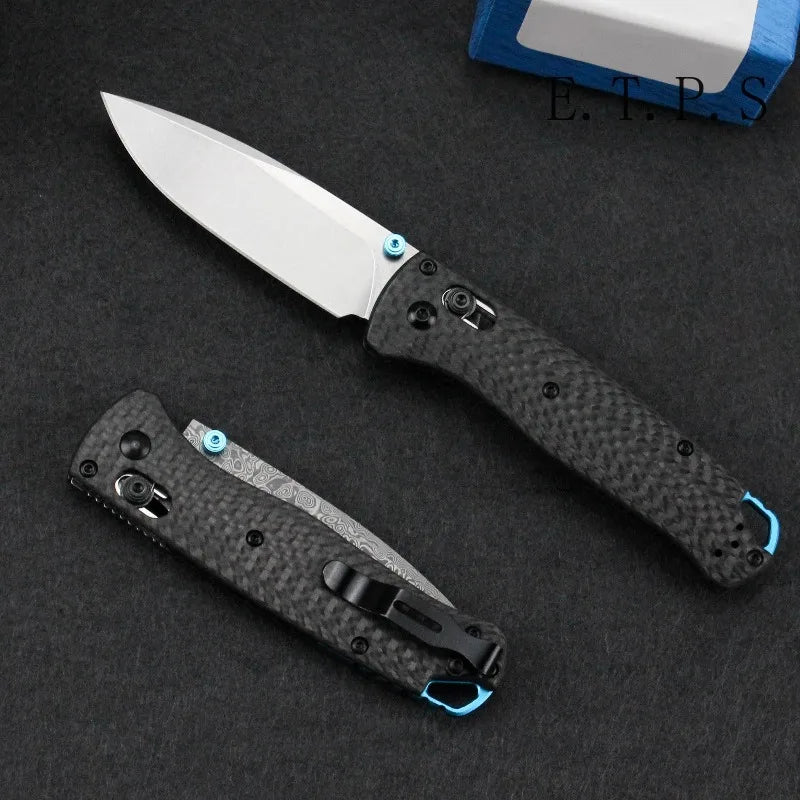 A silver folding hunting knife with a black carbon fiber handle and a white blade is displayed on a dark surface.