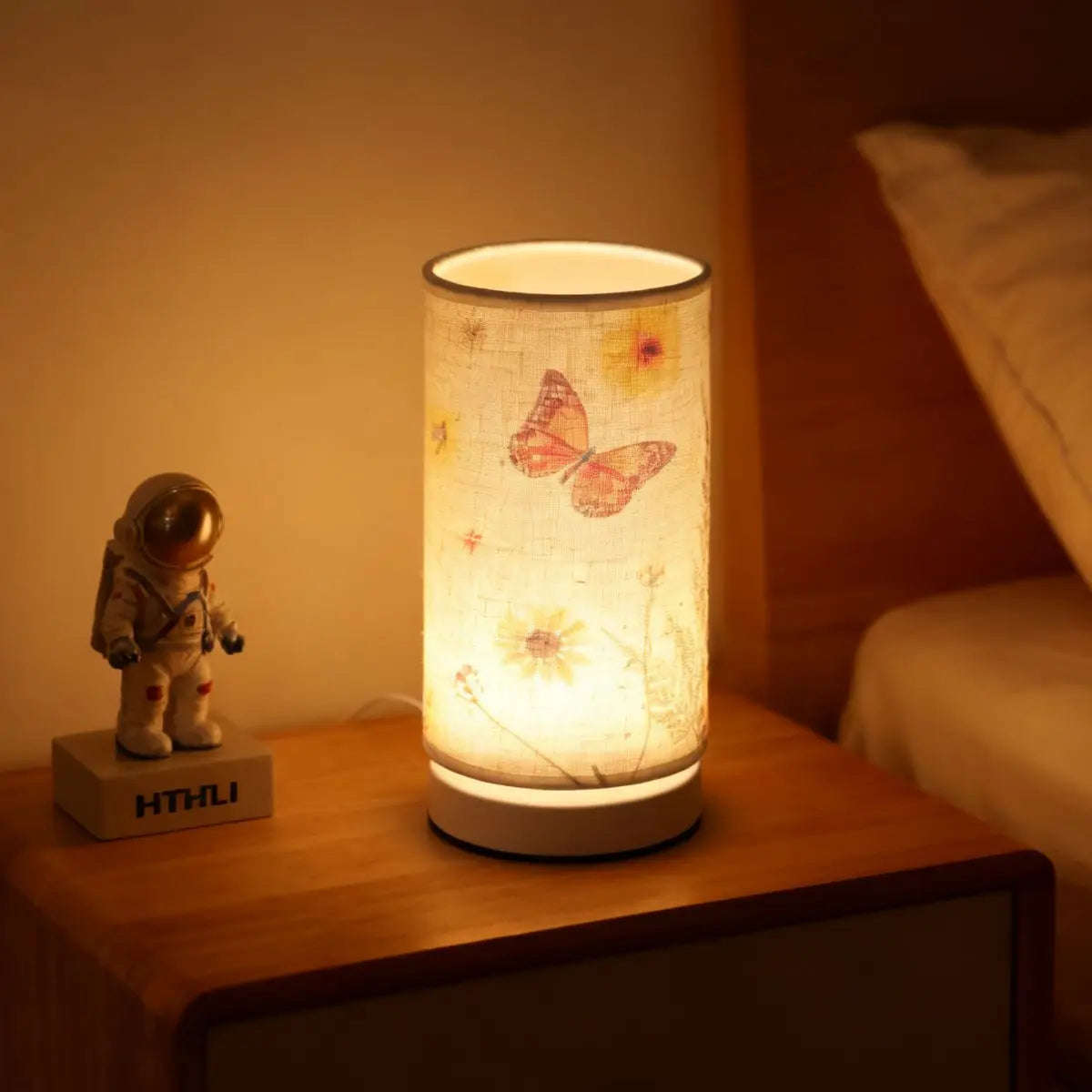 A retro style table lamp with a fabric shade emits a warm glow on a wooden surface.