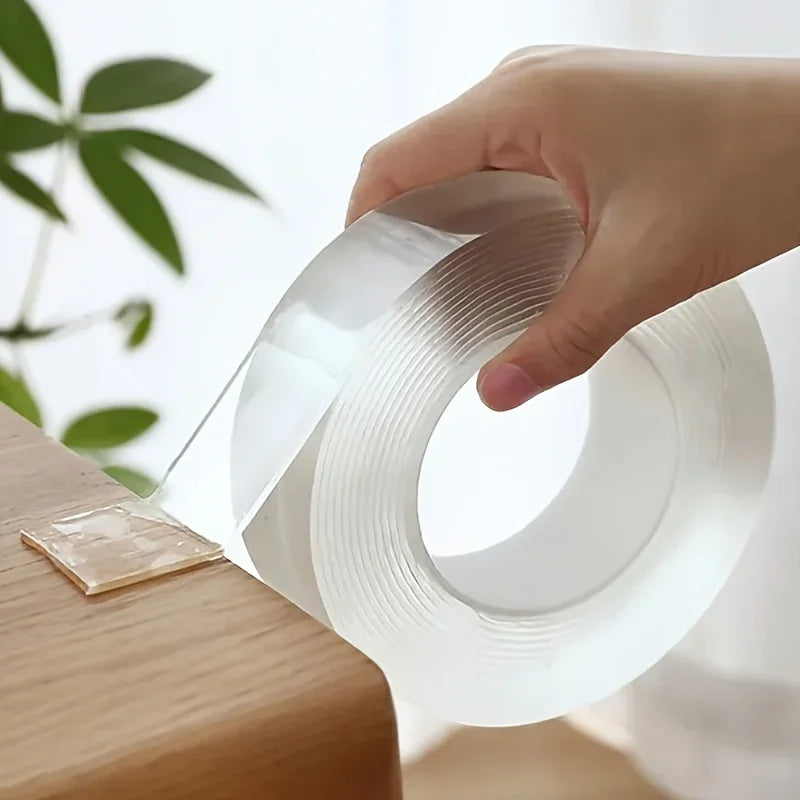 A hand is holding a roll of clear double-sided removable mounting tape against a wooden surface.