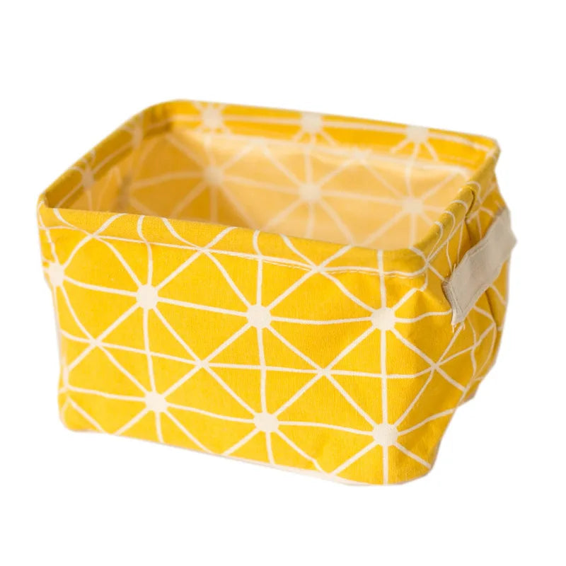 A yellow foldable linen storage basket with a geometric pattern and light beige handles.