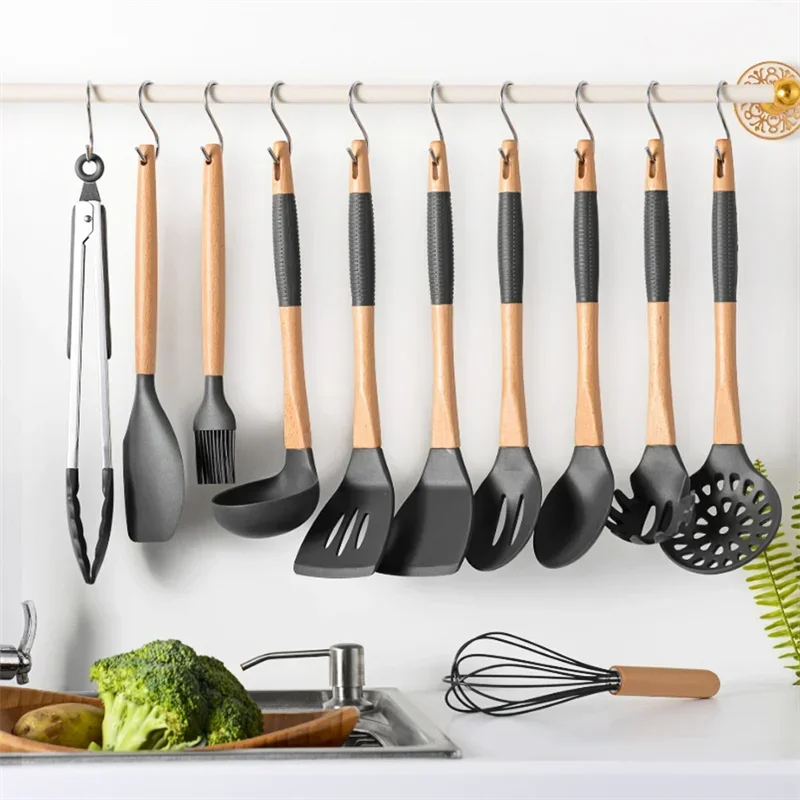 A set of stainless steel hanging kitchen utensils including spatulas and a whisk displayed on a white rack.