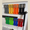 A row of magnetic spray can holders in various colors including gray, yellow, orange, and black mounted on a white panel.