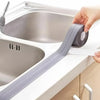 Una mano aplica una bobina de cinta adhesiva impermeable gris para sellar el desagüe de un fregadero blanco de cocina.