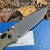 A gray folding EDC pocket knife with a visible blade resting on a blue surface.